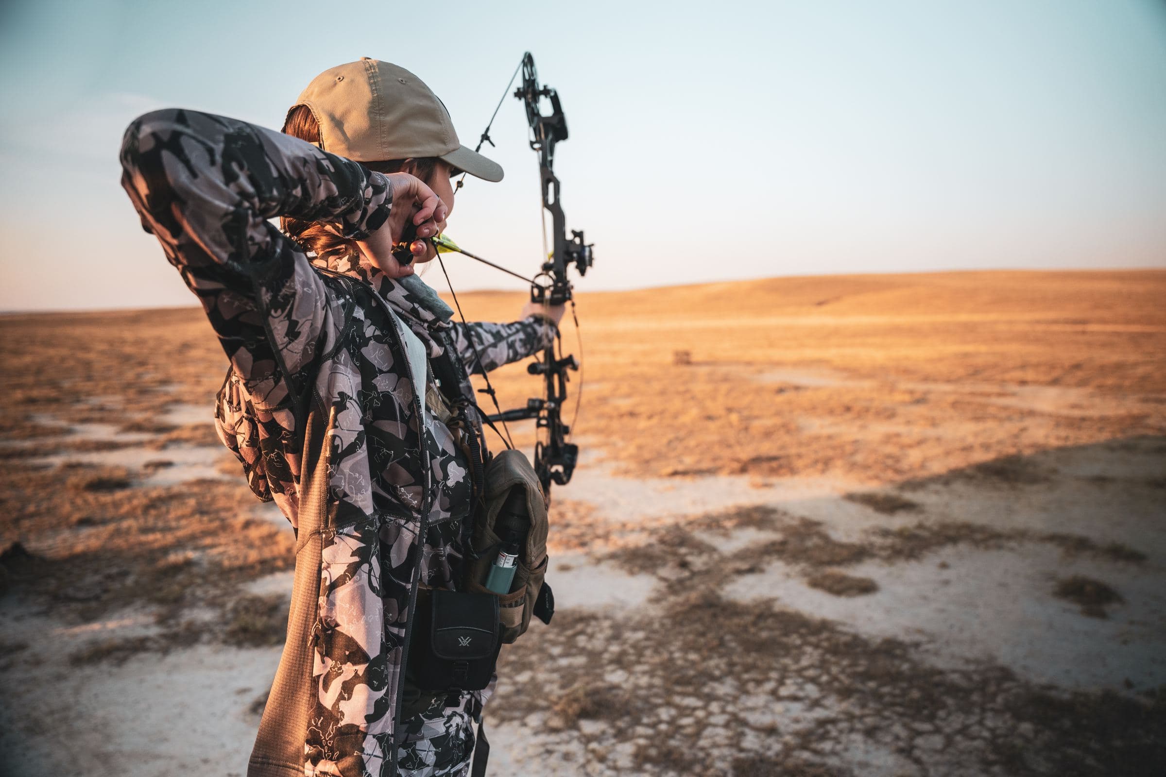 Archer nocks an arrow in warm evening light over golden plains