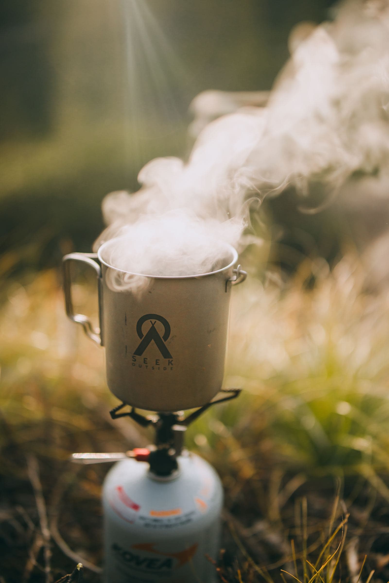 Steam rises from a titanium cup on a backpacking stove in the grass