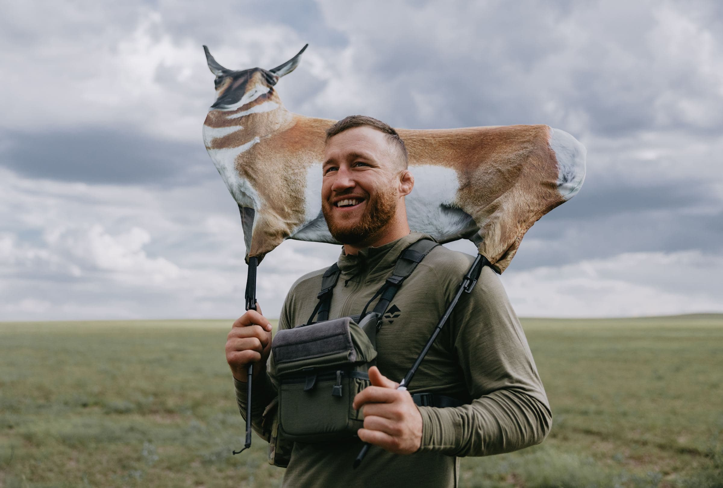 Grinning hunter with a pronghorn carcass draped over his head and shoulders