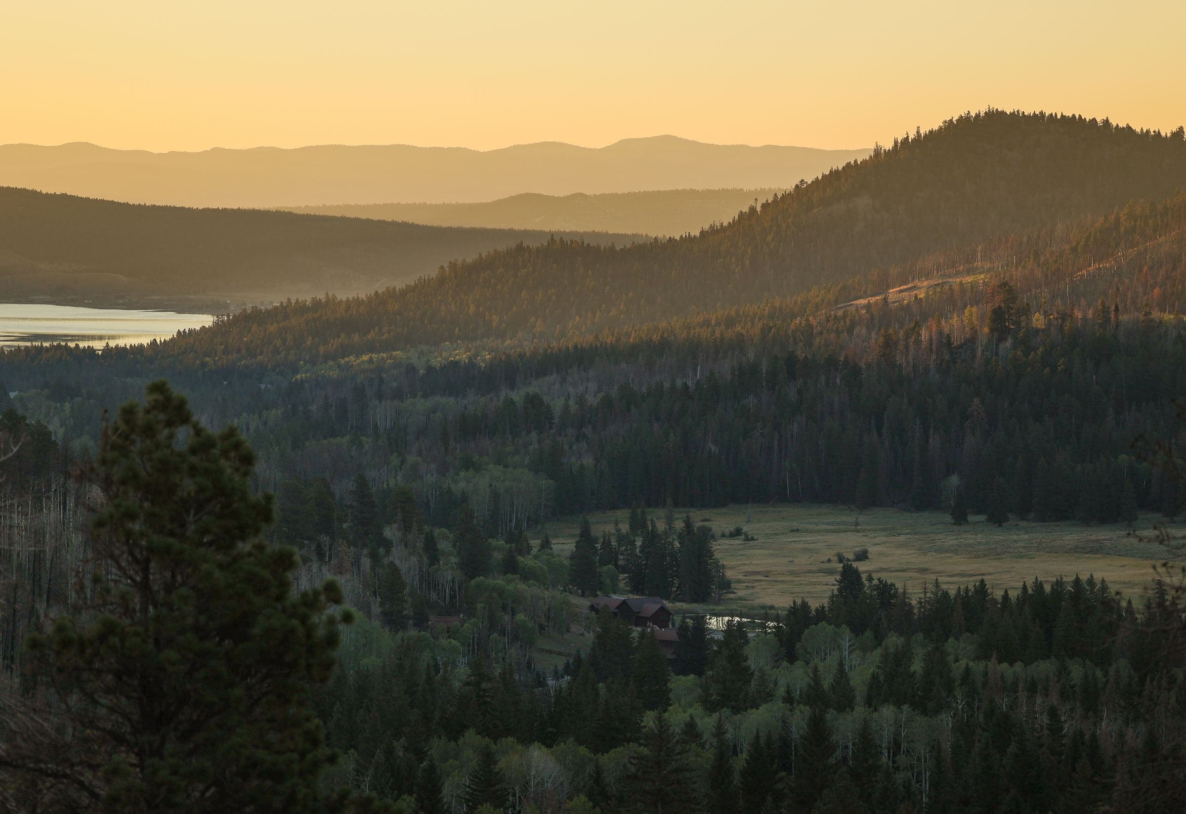 Forested hills and a distant lake under a soft dusk sky
