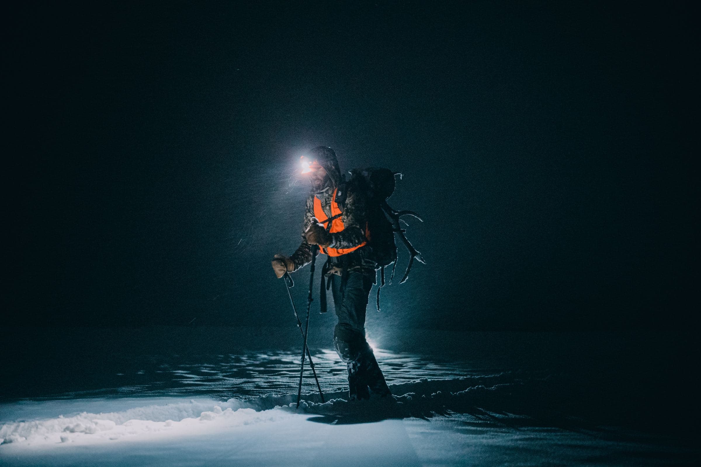Hunter with a headlamp and trekking poles hikes through snow at night