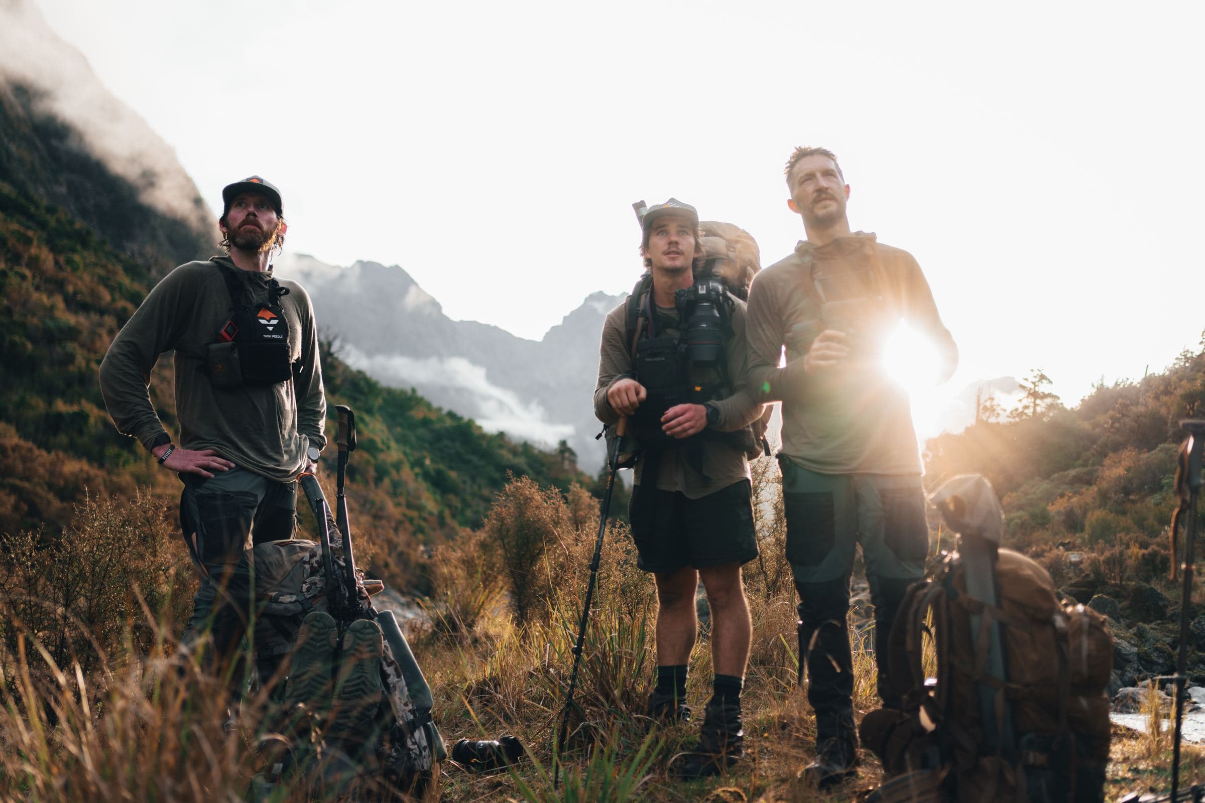 Hunters chat on a backlit mountain slope during a break