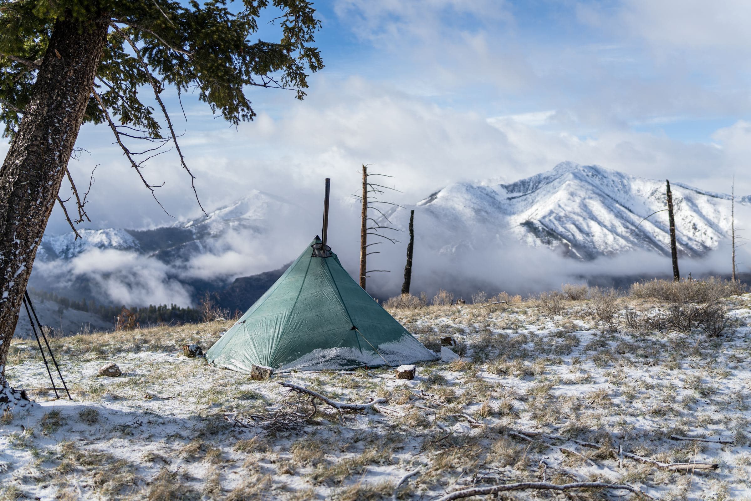 Green tent pitched on a snowy ridge with white mountains behind