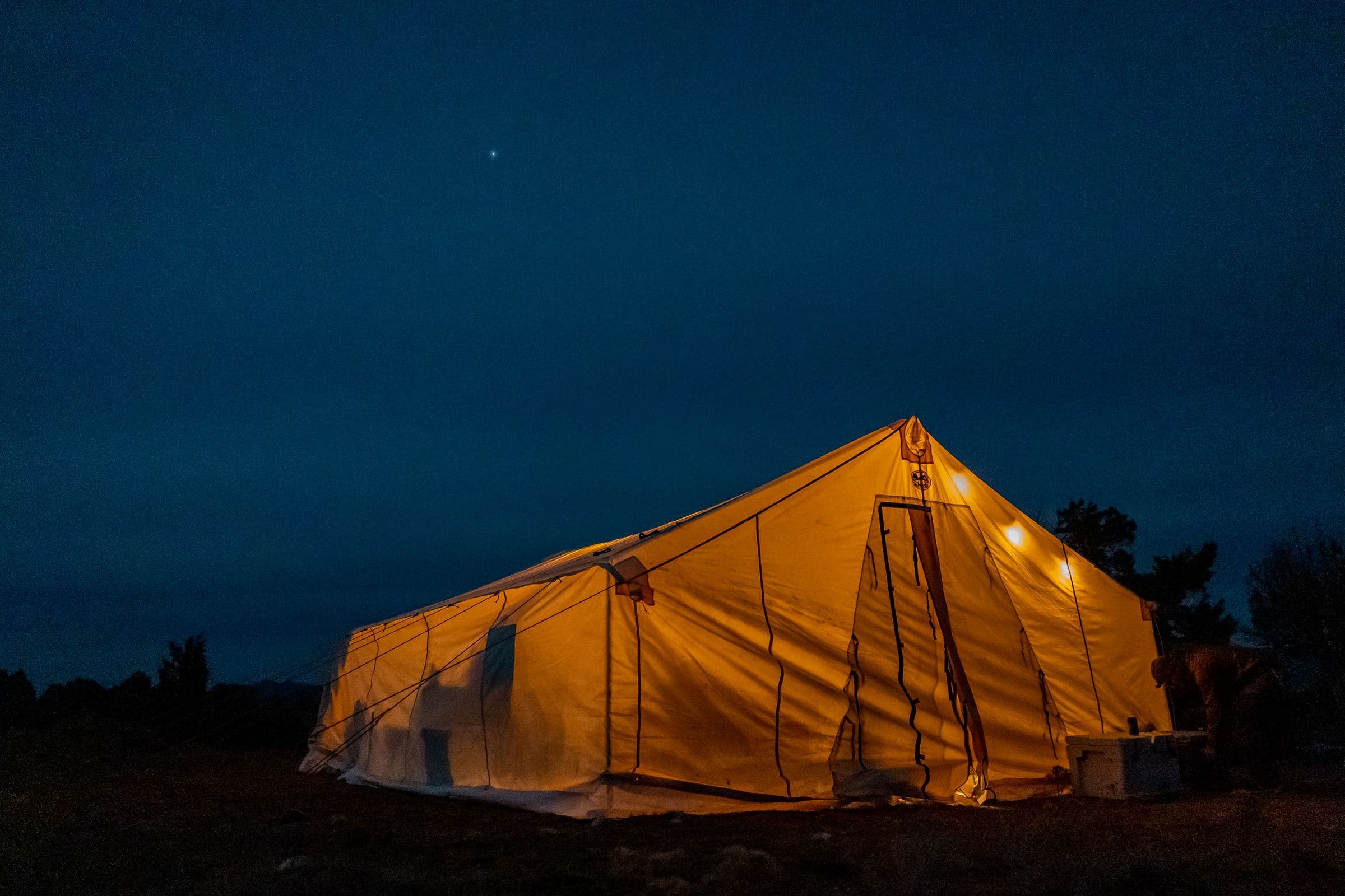 Glowing canvas wall tent at night under a dark blue sky